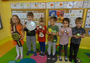 Sześcioro dzieci stoi pod tablicami, w ręku trzymają różne zegary.